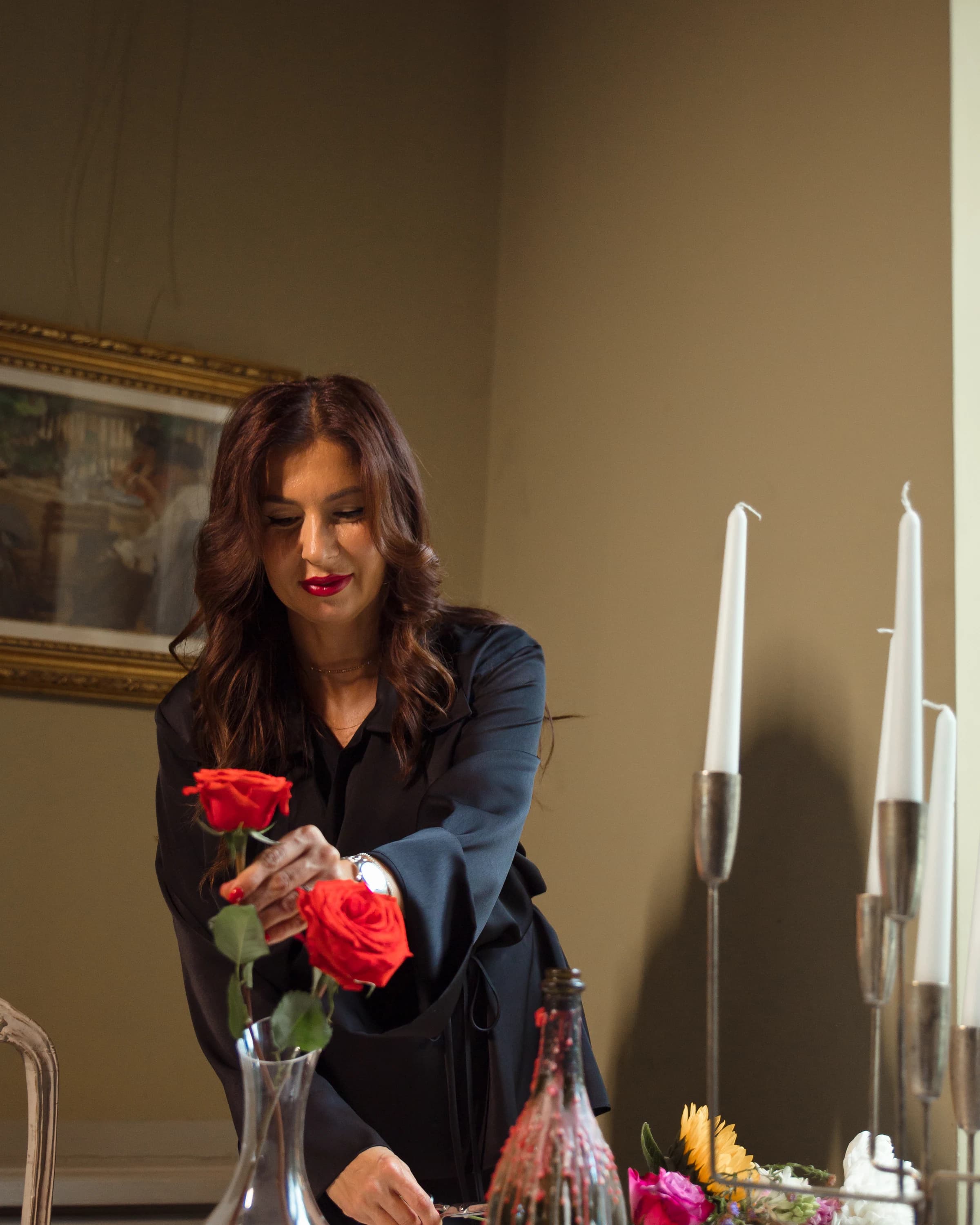 Roxana aranjează trandafiri roșii pe o masă rotundă cu sfeșnice și lumânări